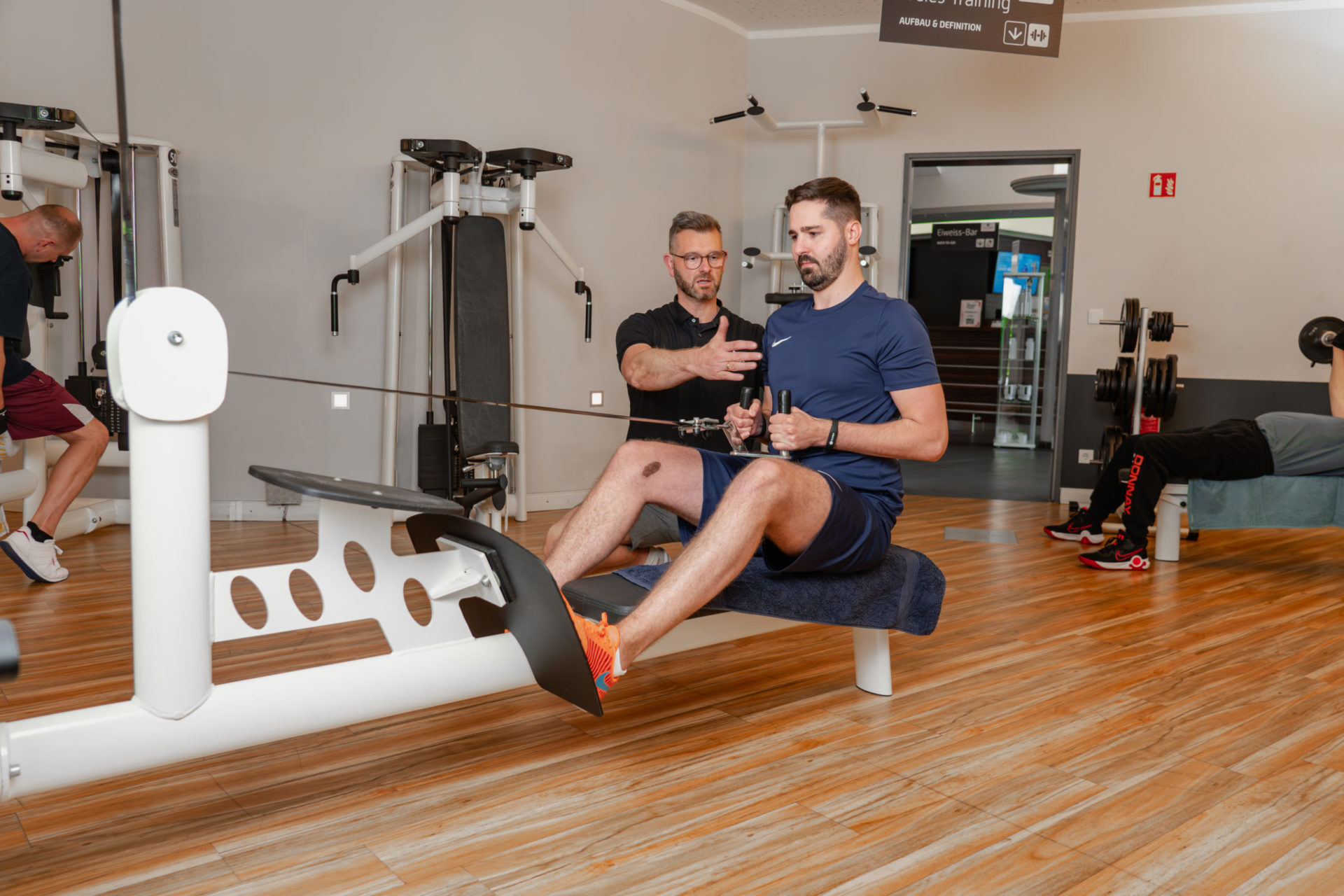 Präzise Betreuung in Bewegung – Ein Coach des LIFE Fitness Oldenburg stellt sicher, dass die Übungsausführung beim tiefen Rudern optimal ist.